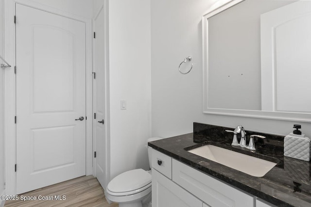 half bathroom with vanity, toilet, and wood finished floors