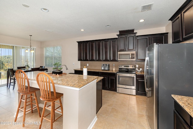 kitchen featuring hanging light fixtures, light stone counters, a notable chandelier, a kitchen island with sink, and appliances with stainless steel finishes