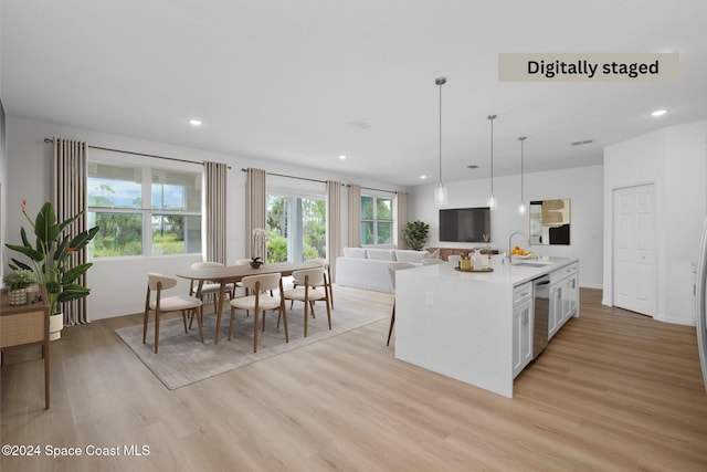 kitchen featuring white cabinetry, dishwasher, light hardwood / wood-style flooring, decorative light fixtures, and a kitchen island with sink