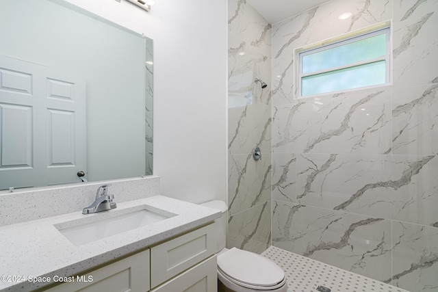 bathroom with a tile shower, vanity, and toilet