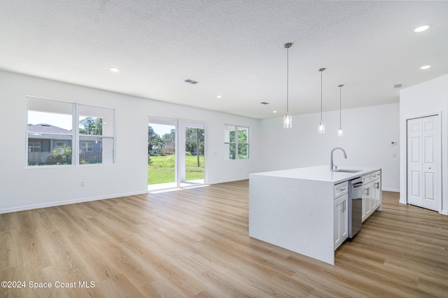 kitchen featuring stainless steel dishwasher, sink, decorative light fixtures, white cabinets, and an island with sink