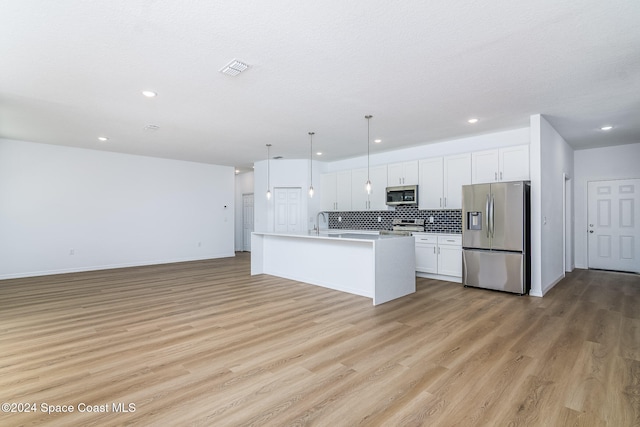 kitchen featuring a center island with sink, light wood-type flooring, appliances with stainless steel finishes, decorative light fixtures, and white cabinetry