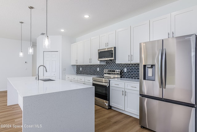 kitchen featuring appliances with stainless steel finishes, sink, pendant lighting, white cabinetry, and an island with sink