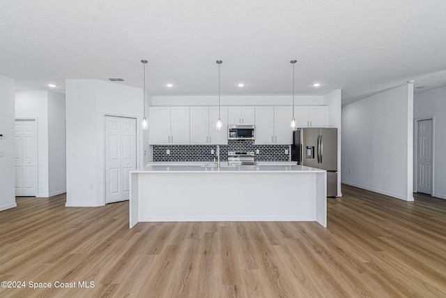 kitchen featuring white cabinets, appliances with stainless steel finishes, pendant lighting, and an island with sink