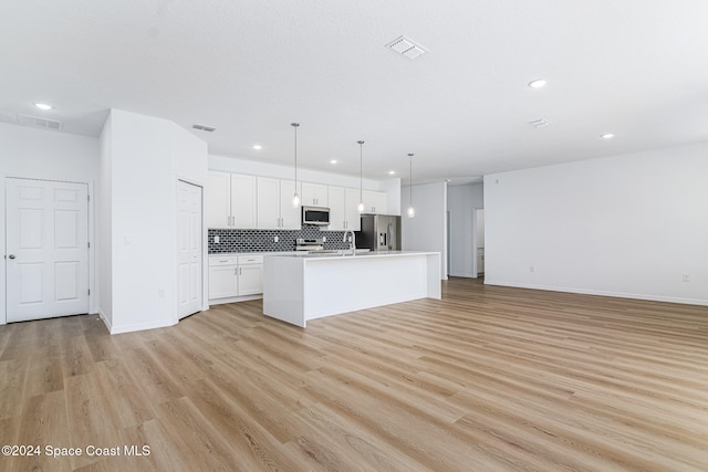 kitchen with backsplash, stainless steel appliances, decorative light fixtures, white cabinets, and an island with sink