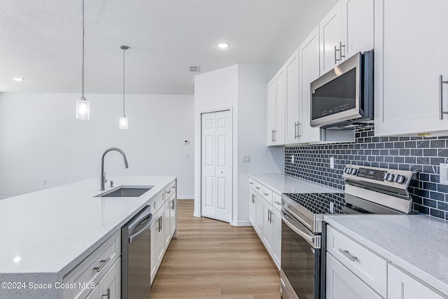 kitchen featuring sink, pendant lighting, decorative backsplash, white cabinets, and appliances with stainless steel finishes