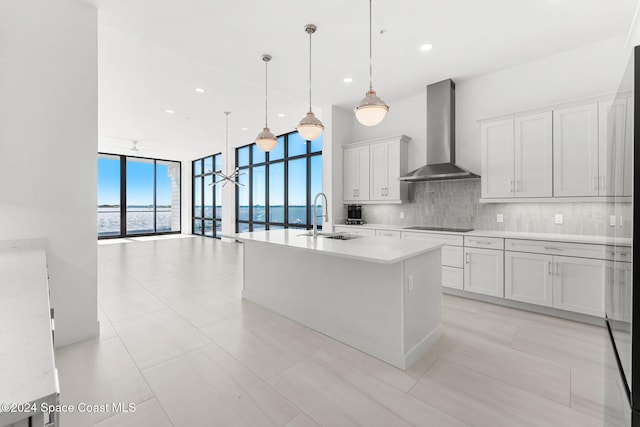 kitchen with a water view, sink, wall chimney exhaust hood, tasteful backsplash, and decorative light fixtures