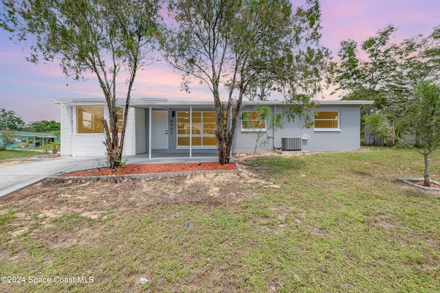 ranch-style house featuring central air condition unit and a yard