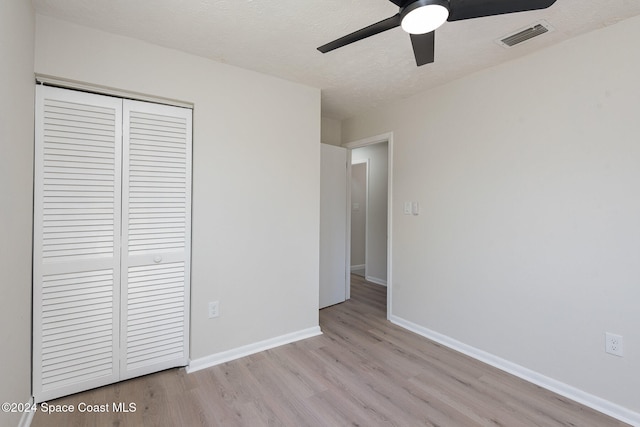 unfurnished bedroom featuring ceiling fan, light wood-type flooring, a textured ceiling, and a closet