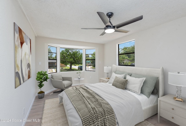 bedroom with a textured ceiling, ceiling fan, multiple windows, and light hardwood / wood-style flooring