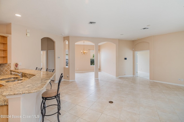 kitchen with light stone countertops, sink, a notable chandelier, backsplash, and light tile patterned floors