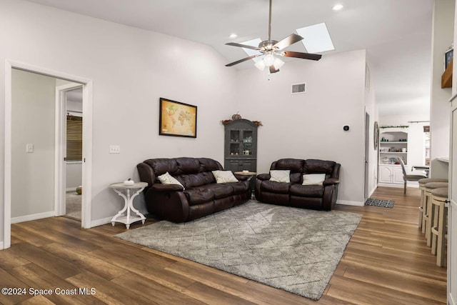 living room with a skylight, ceiling fan, dark hardwood / wood-style flooring, and high vaulted ceiling