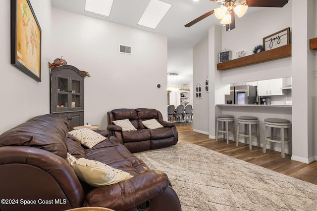 living room featuring a towering ceiling, a skylight, ceiling fan, and dark wood-type flooring