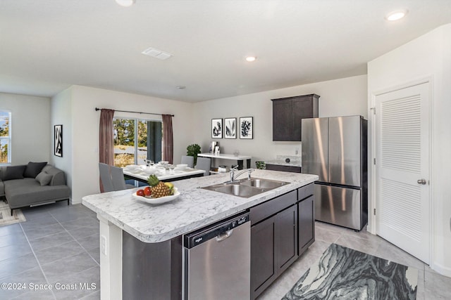 kitchen with a kitchen island with sink, sink, light tile patterned flooring, dark brown cabinetry, and stainless steel appliances