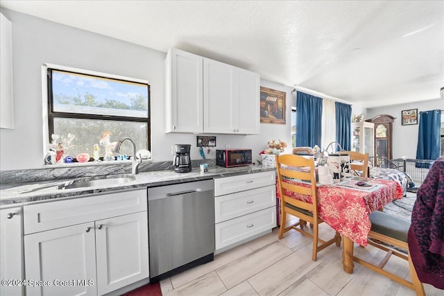 kitchen featuring stainless steel dishwasher, light stone counters, sink, light hardwood / wood-style flooring, and white cabinetry