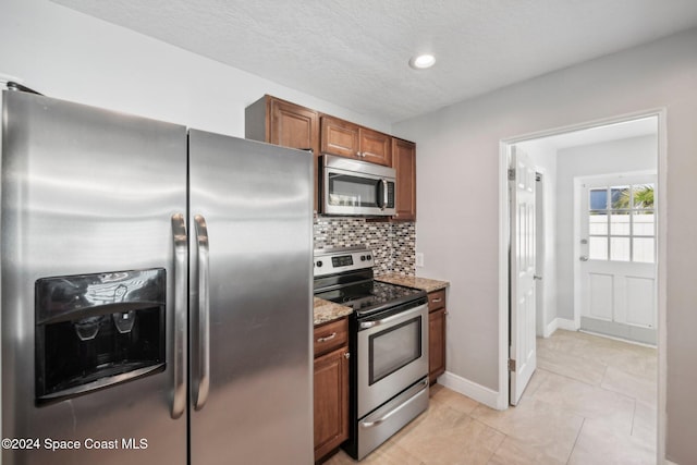 kitchen with light stone countertops, stainless steel appliances, backsplash, a textured ceiling, and light tile patterned flooring