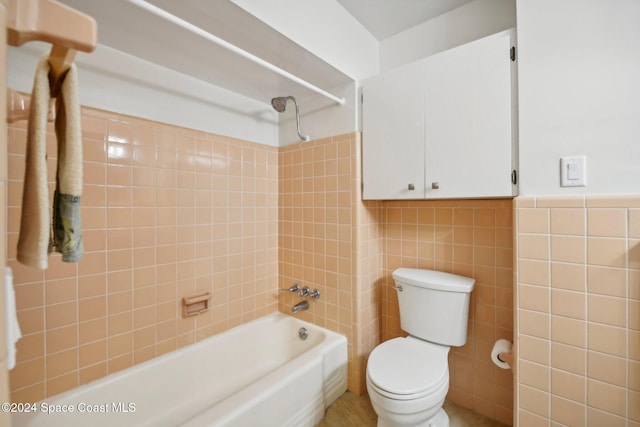 bathroom with tiled shower / bath combo, toilet, and tile walls