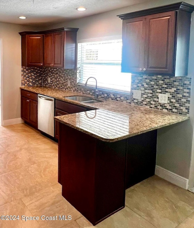 kitchen featuring backsplash, sink, stainless steel dishwasher, a textured ceiling, and kitchen peninsula