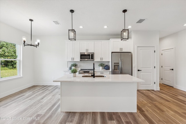 kitchen featuring white cabinetry, pendant lighting, stainless steel appliances, and a center island with sink