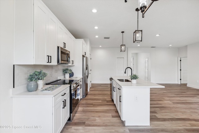 kitchen featuring pendant lighting, appliances with stainless steel finishes, white cabinets, sink, and a kitchen island with sink