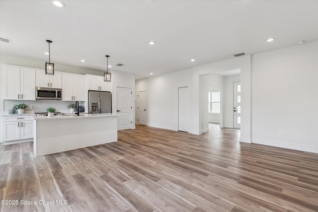 kitchen featuring hanging light fixtures, white cabinets, a center island with sink, and stainless steel appliances