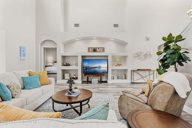 living room with built in shelves, wood-type flooring, and a towering ceiling