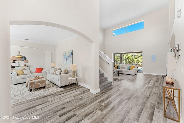 living room with ornamental molding, a towering ceiling, and light hardwood / wood-style flooring