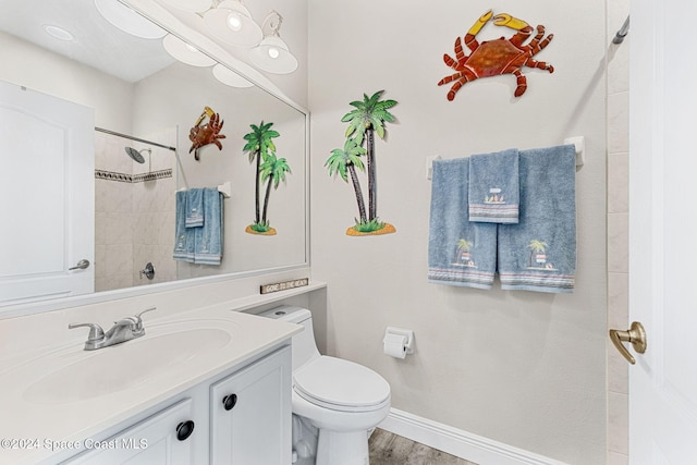 bathroom with tiled shower, toilet, vanity, and hardwood / wood-style flooring