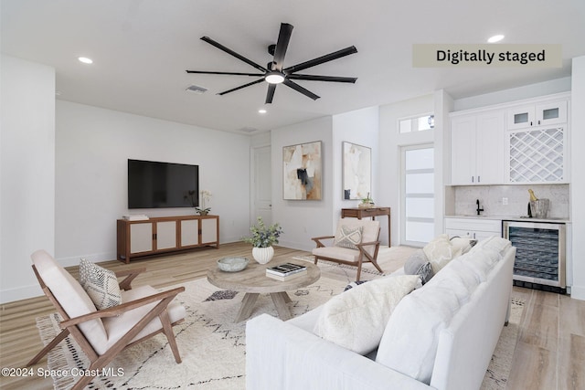 living room with bar, ceiling fan, beverage cooler, and light hardwood / wood-style flooring