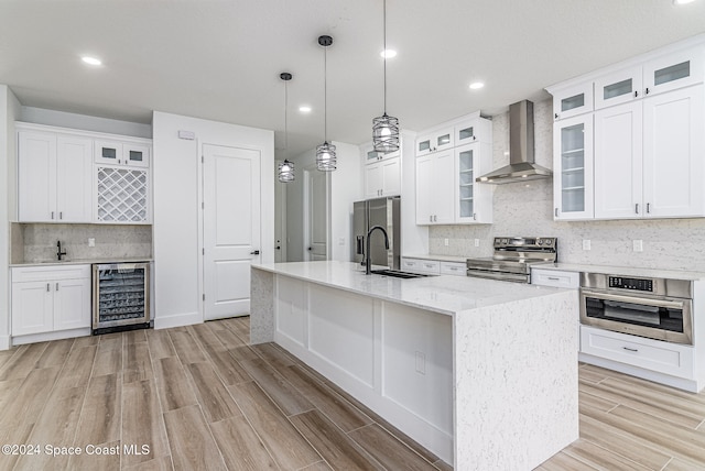 kitchen with stainless steel appliances, a kitchen island with sink, beverage cooler, sink, and wall chimney range hood