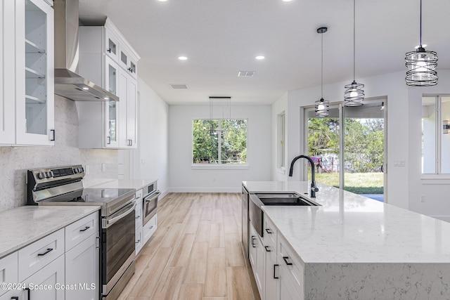 kitchen featuring a kitchen island with sink, sink, wall chimney exhaust hood, white cabinetry, and stainless steel appliances