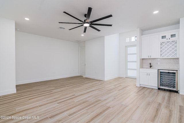 unfurnished living room with bar area, light wood-type flooring, wine cooler, and ceiling fan