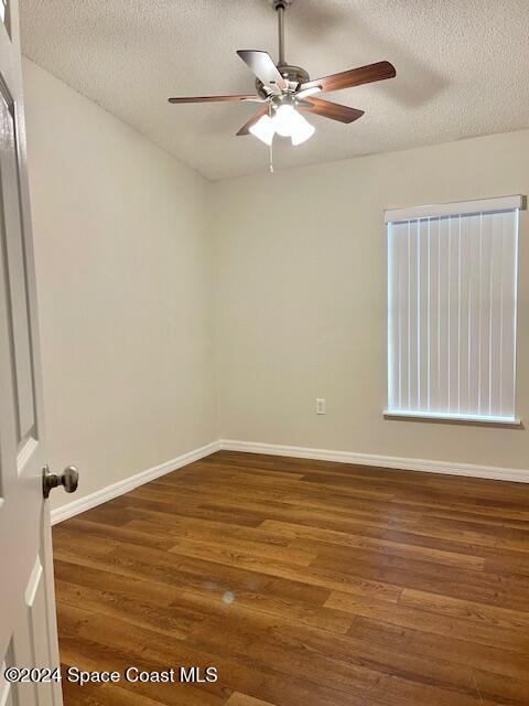 spare room with a textured ceiling, ceiling fan, and dark wood-type flooring