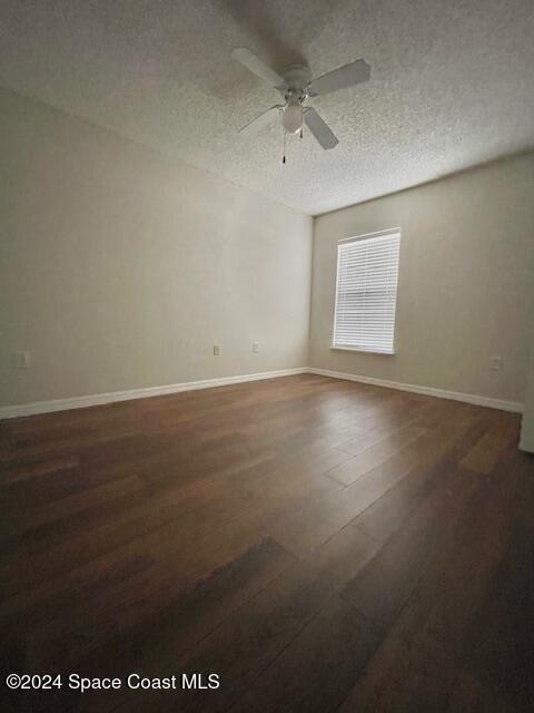 unfurnished room featuring a textured ceiling, ceiling fan, and dark wood-type flooring