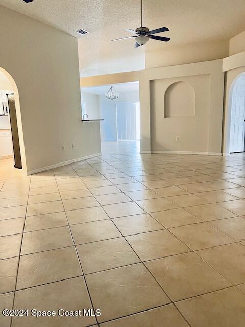 unfurnished room featuring ceiling fan with notable chandelier, light tile patterned floors, and a textured ceiling