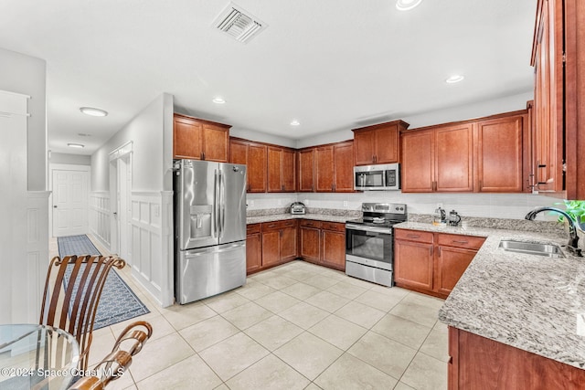 kitchen with light stone countertops, appliances with stainless steel finishes, light tile patterned floors, and sink