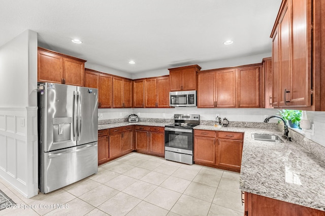 kitchen with light stone countertops, light tile patterned floors, stainless steel appliances, and sink