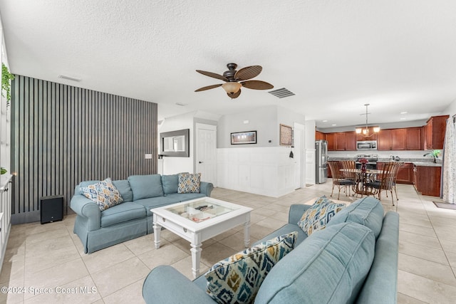 living room with light tile patterned flooring, a textured ceiling, ceiling fan with notable chandelier, and sink