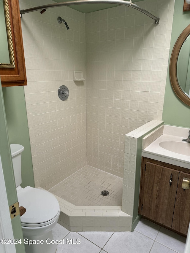 bathroom with toilet, a tile shower, vanity, and tile patterned floors