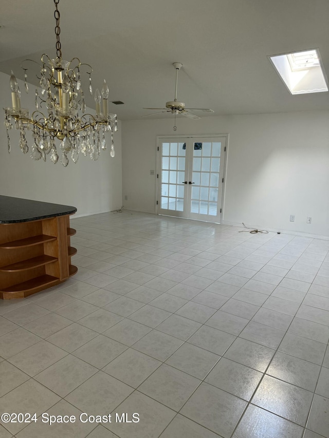 empty room featuring vaulted ceiling with skylight, light tile patterned floors, and ceiling fan with notable chandelier