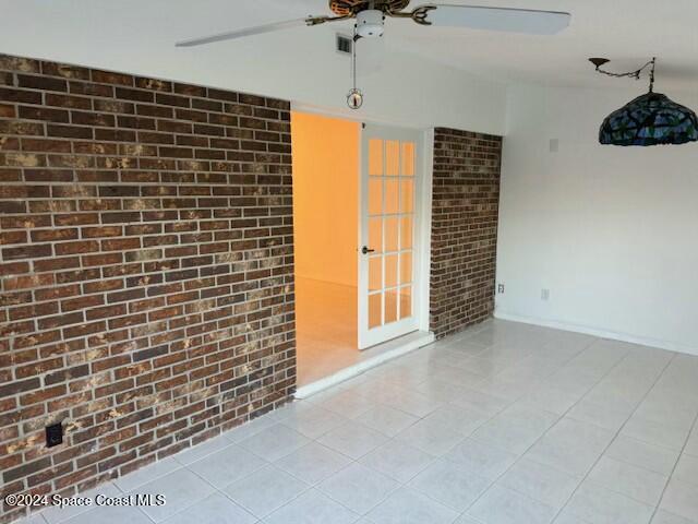 spare room featuring ceiling fan and brick wall