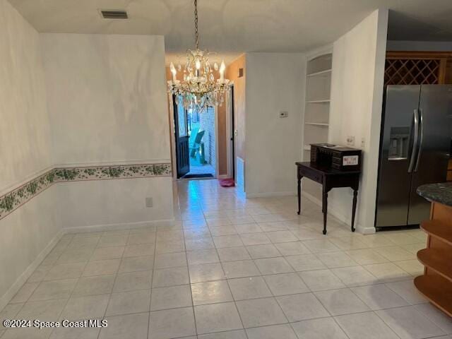 unfurnished dining area with built in features, light tile patterned floors, and a chandelier