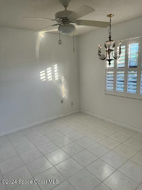 empty room featuring ceiling fan with notable chandelier and light tile patterned flooring