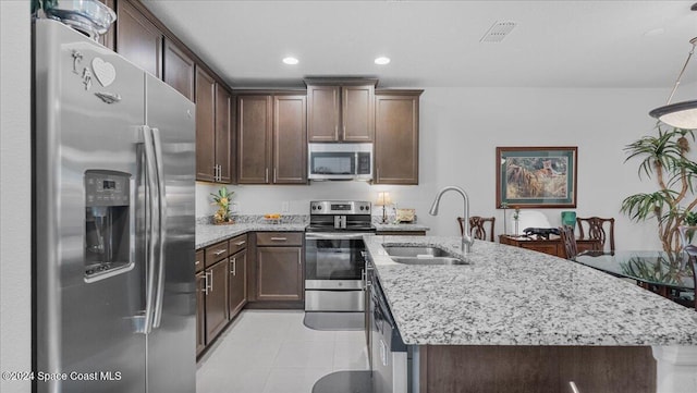 kitchen with a kitchen island with sink, light stone countertops, sink, and appliances with stainless steel finishes