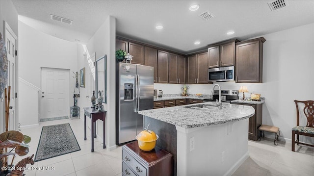 kitchen featuring light stone counters, stainless steel appliances, a kitchen island with sink, sink, and light tile patterned flooring