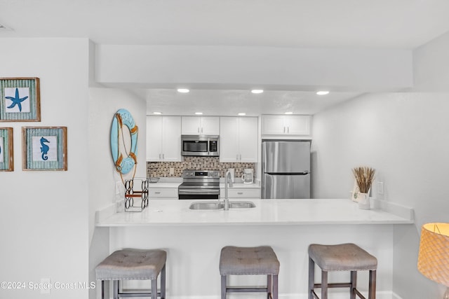 kitchen featuring kitchen peninsula, appliances with stainless steel finishes, a breakfast bar, sink, and white cabinets