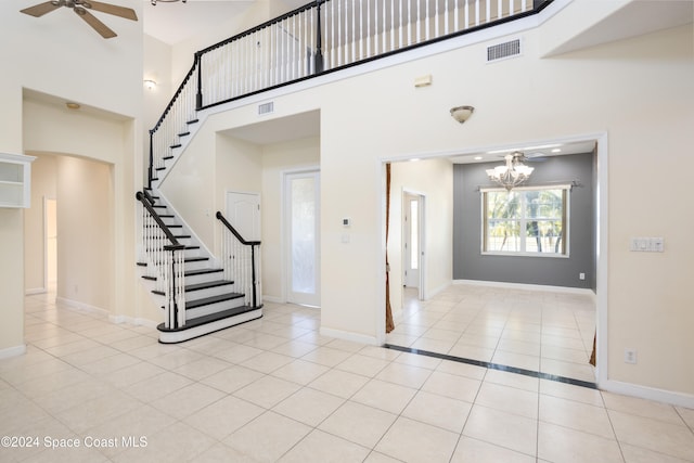 foyer with ceiling fan with notable chandelier, light tile patterned flooring, and a towering ceiling