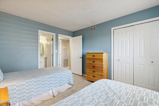 bedroom with a textured ceiling, light hardwood / wood-style floors, a closet, and ensuite bathroom