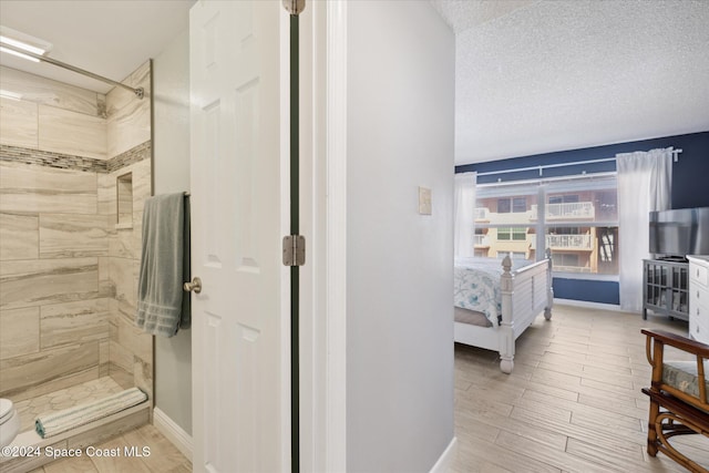 bathroom with hardwood / wood-style floors, toilet, a tile shower, and a textured ceiling