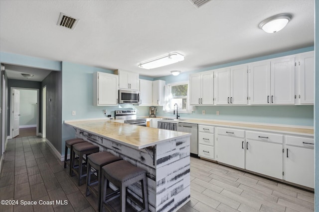 kitchen featuring a kitchen breakfast bar, white cabinetry, stainless steel appliances, and light hardwood / wood-style floors